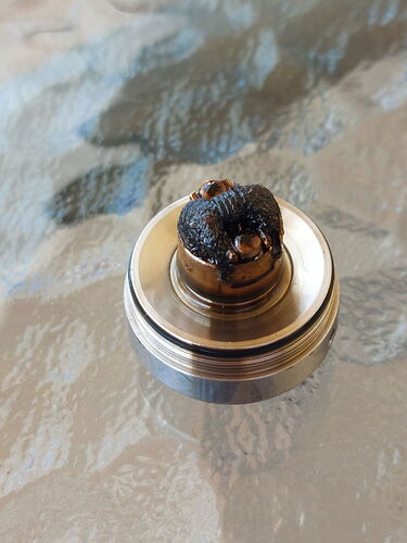 The image shows a metal part with a carbonized, soot-covered coil or insulating material in the middle. (Labeled by AI)