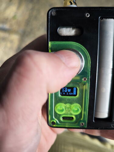 A hand presses a button on a black and green electronic device, which has a small blue display. (Labeled with AI)