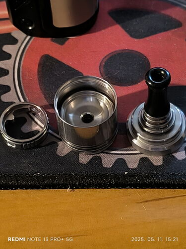 The image depicts a disassembled metal device, likely showing parts of a smoking or vape accessory. (Labeled by AI)