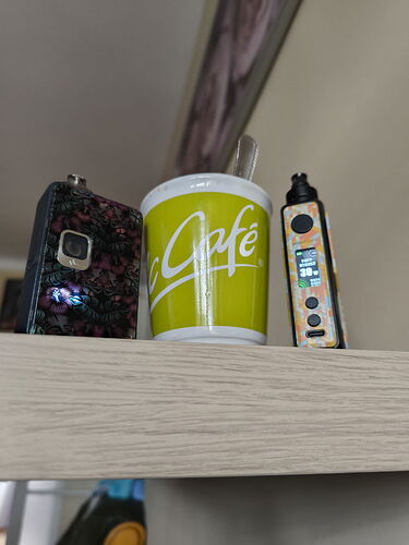 Two vape devices and a yellow coffee cup are visible on a light wooden shelf. (Labeled by AI)