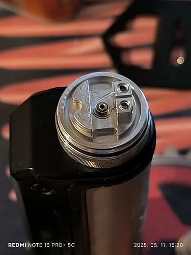 The image shows a detail of an electronic cigarette (vape) with a metal-structured atomizer on top. (Labeled by AI)