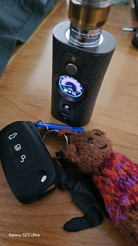 A cigarette, a car key, a crocheted bear and a small black figure are visible on the table. (Captioned by AI)