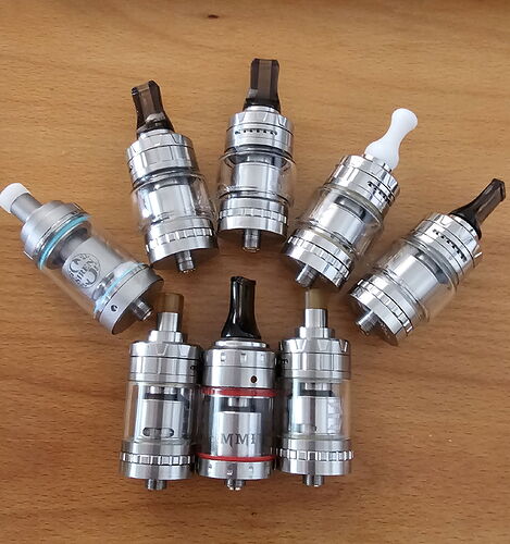 Eight different metal electronic cigarette tanks are arranged on the table. (Captioned by AI)