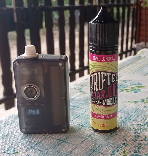 A dark gray vaping device stands next to a bottle of lemon and lime flavored Drifter Bar Juice e-liquid on a patterned table. (Labeled by AI)