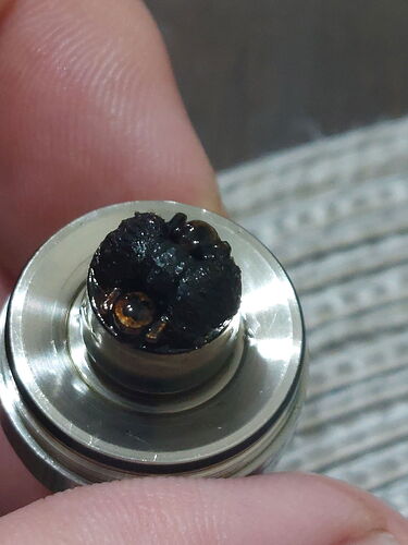 A hand holds a metal vaping coil with a heavily burnt and discolored wick. (Labeled by AI)