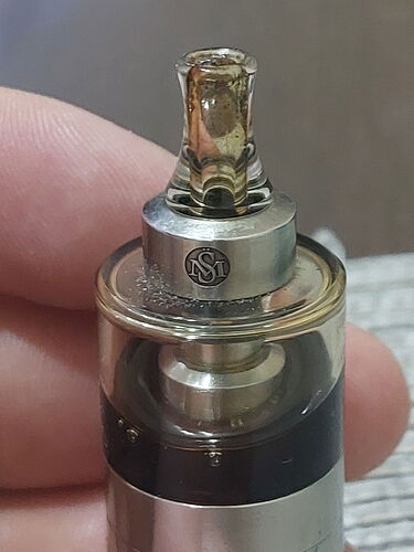 Top view of a silver vape device held by a hand, featuring a transparent, ornate drip tip. (Labeled by AI)