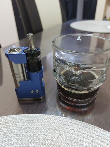 A blue vaporizer and a glass of dark drink are on the table. (Subtitled by AI)