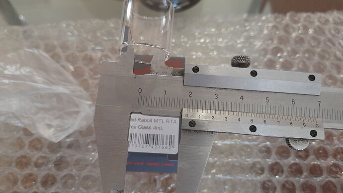 Egy tolómérővel lemérnek egy dobozt, amelyen az Red Rabbit MTL RTA felirat olvasható. (Feliratozva AI-val)