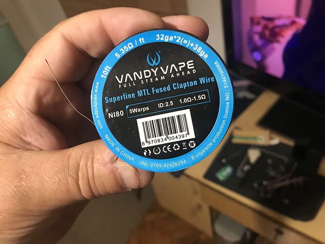 Egy kézben egy Vandy Vape Superfine MTL Fused Clapton Wire csomagja látható, amelyet e-cigaretta tekercseléséhez használnak. (Feliratozva AI-val)