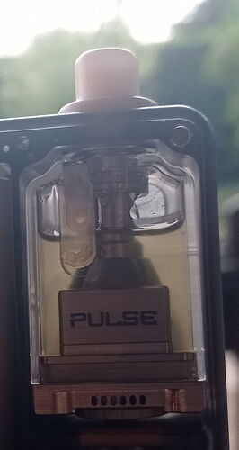 A close-up of an e-cigarette liquid tank, labeled "PULSE", with a transparent wall showing yellowish liquid and internal mechanics. (Labeled by AI)