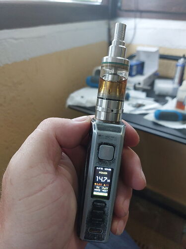 An electronic cigarette device held in one hand in an indoor environment, with a worktop and various tools visible in the background. (AI-generated caption)