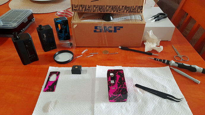 Parts of a disassembled pink plasma patterned Stubby and various tools are visible on a table in front of a background full of boxes.
