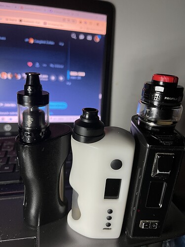 Az ábrán három különböző vape eszköz látható, amelyeket egy laptop háttérvilágítása mellett helyeztek el. (Feliratozva AI-val)