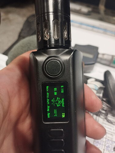 A képen egy kézben tartott elektronikusan vezérelt vape eszköz látható, amely kijelzőjén különböző beállítási információk és értékek olvashatók. (Feliratozva AI-val)