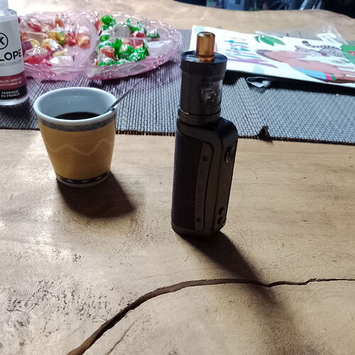 A coffee cup and an electronic cigarette are on a table, with sweets and a book in the background. (AI-captioned)