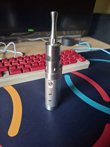 Egy ezĂŒst szĂnƱ, henger alakĂș e-cigaretta ĂĄllĂtĂłlag a szĂĄmĂtĂłgĂ©pes billentyƱzet elĆtt egy asztalon. (Feliratozva AI-val)