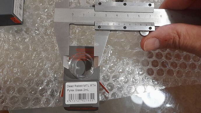 Egy kéz egy tolómérővel méri egy Dead Rabbit MTL RTA Pyrex Glass 2mL tartály üvegének átmérőjét buborékfólián fekve. (Feliratozva AI-val)