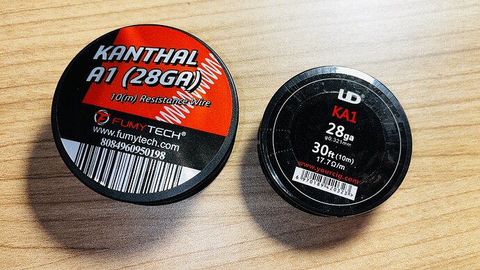 On the table, two spools of Kanthal A1 28GA resistance wire are visible, one larger FumyTech brand and one smaller UD brand. (Labeled by AI)
