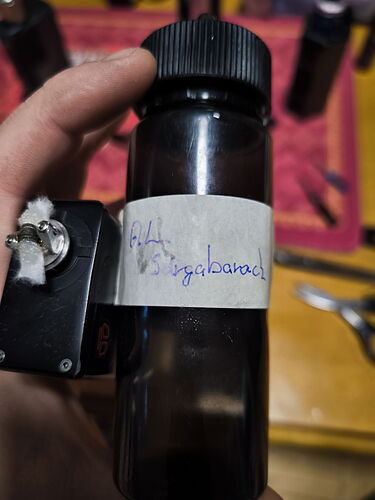 A hand holding a round black-capped bottle with a handwritten paper label that reads 'ZdA sziglabacai'. (Caption provided by AI)