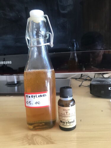 A bottle of liquid and a small bottle labeled Maryland concentrate, on a table, with a Samsung screen in the background. (Labeled by AI)
