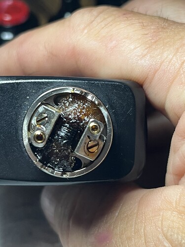 A hand holding a black electronic smoking device (vape) with its heating chamber visible and filled with burnt material. (Captioned by AI)