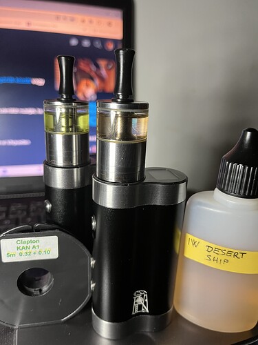 Deux vaporisateurs et une bouteille de liquide nicotiné sont visibles sur la photo, tandis qu'un écran d'ordinateur apparaît en arrière-plan. (Sous-titré par IA)