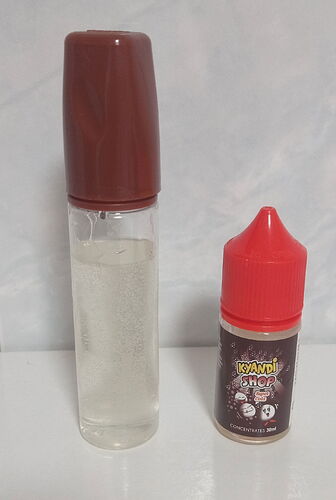 Egy átlátszó folyadékot tartalmazó, barna kupakkal ellátott műanyag flakon és egy kis méretű, piros kupakkal rendelkező 30 ml-es e-liquid koncentrátum flakon áll egymás mellett. (Feliratozva AI-val)