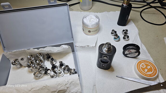 Sur la table se trouvent diverses pièces métalliques, un module de cigarette électronique, un pot de crème et une boîte ronde placés sur des lingettes blanches. (Légendé par l'IA)