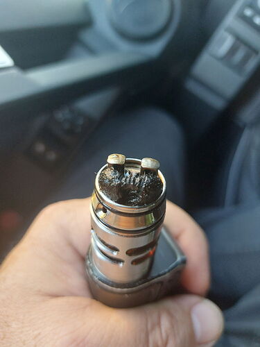 A hand holding the atomizer head of an e-cigarette (vape), which has burnt cotton strands. (Subtitled with AI)