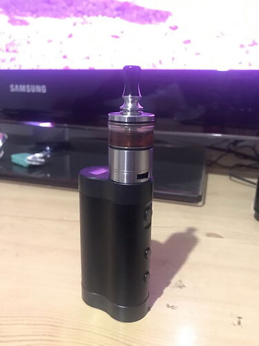 The image shows a black e-cigarette standing next to the TV in the background. (Captioned by AI)