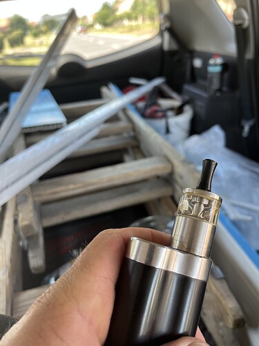 Une main tenant une cigarette électronique à l'intérieur d'une voiture, où un escabeau et quelques objets sont visibles. (Légendé par IA)