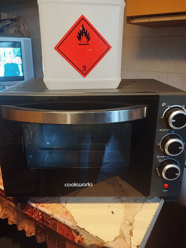 Un micro-ondes de marque Cookworks et un récipient indiquant un matériau inflammable sont visibles dans une cuisine. (Légendé par IA)