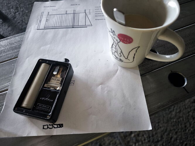 Un dessin et un régulateur sont sur une feuille de papier sur une table en bois, à côté d'une tasse de café et d'un petit couvercle. (Sous-titré par IA)