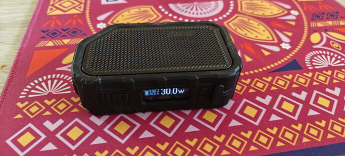 Un appareil électronique noir avec un écran numérique est placé sur une nappe colorée ornée de motifs géométriques. (Légendé par IA)