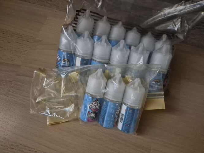 Diverses petites bouteilles en plastique, contenant probablement des liquides, sont placées dans un emballage en plastique transparent sur un plancher en bois. (Étiqueté par IA)