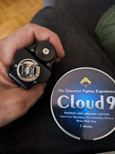 A hand holds an open vaporizer device next to a box of "Cloud 9" organic cotton. (AI-captioned)