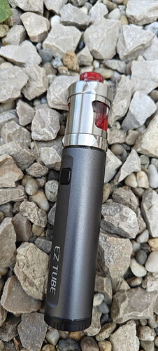 A silver-black EZ TUBE e-cigarette with a red mouthpiece lies among pebbles. (Subtitled with AI)