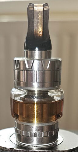 The image shows a metal and glass part, depicting an electronic cigarette tank and atomizer. (Labeled by AI)