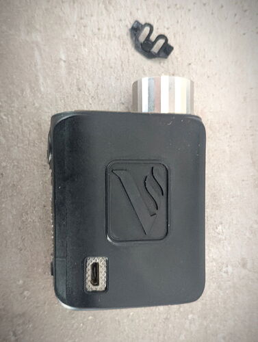 The image shows a black vape device with a USB connector on its side, and a smaller component is also visible next to it. (AI-generated caption)