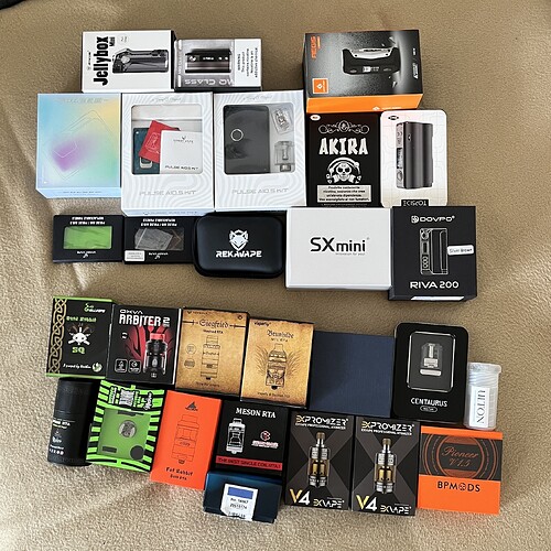 La photo montre des boîtes de divers appareils et accessoires de vape, placées sur une surface gris clair. (Légendé par IA)