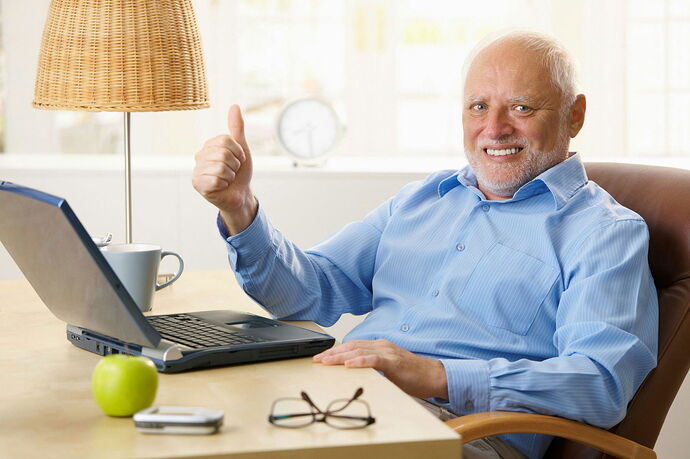 An elderly man smiling and giving a thumbs up sitting at a desk in front of a laptop, with a green apple and a cup of coffee nearby. (captioned by AI)