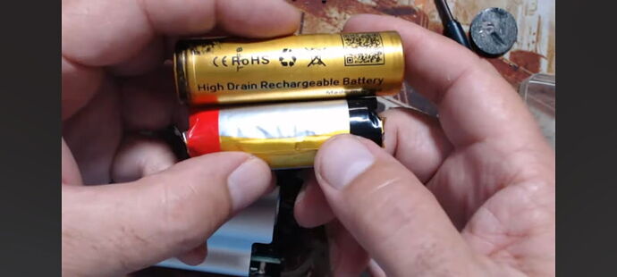 L'image montre deux batteries, dont l'une est dorée et porte l'inscription "High Drain Rechargeable Battery". (Sous-titré par IA)