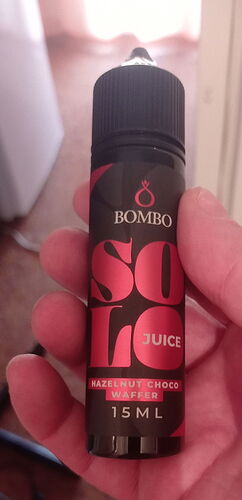 A hand holding a black bottle labeled "Bombo Solo Juice Hazelnut Choco Waffer 15 ML". (Labeled by AI)