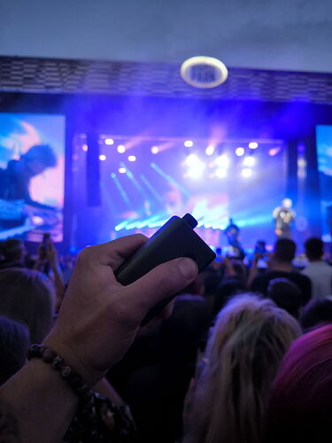 Egy koncert közönsége előtt egy kéz látható, amely egy öngyújtót tart fel a színpad felé világítva. (Feliratozva AI-val)