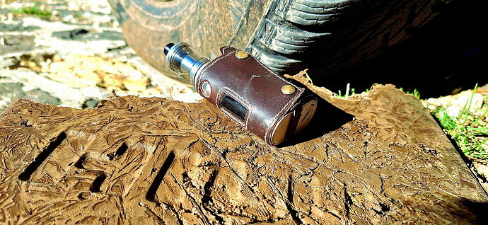 The image shows a brown leather-cased vape device lying on a wooden surface, with a car wheel behind it. (Labeled by AI)