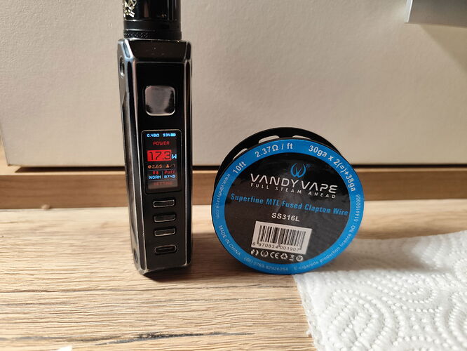 A coil and an e-cigarette device from the Vandy Vape brand are visible on a wooden surface. (Subtitled by AI)