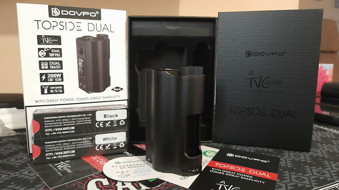 Sur cette photo, un appareil de cigarette électronique DOVPO Topside Dual de couleur noire, son emballage, ainsi que les manuels d'utilisation et accessoires sont visibles. (Légendé par IA)