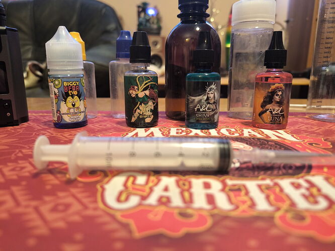 Bottles containing various vaper liquids and a syringe are visible on the table. (Captioned by AI)