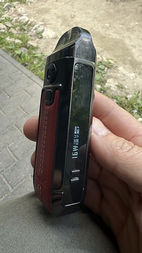 Egy kézben tartott, digitális kijelzővel és bőrborítással rendelkező vape eszköz látható egy kültéri környezetben. (Feliratozva AI-val)