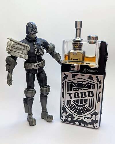 An action figure dressed as a court judge stands next to a metal box labeled "TODD". (Autocaptioned)